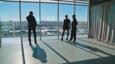 Erkek girişimci takım elbiseli, telefonlu ve kadın kapalı mekanlı. Güzel bayan ortaklar pencerenin yanında duran bir iş adamına el sallıyor..