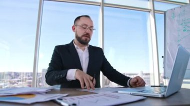 Görevde başarılı bir girişimci konuşuyor. Gözlüklü ve şık takım elbiseli bir işadamı iş yerindeki masada oturmuş ciddi bir şekilde konuşuyor..