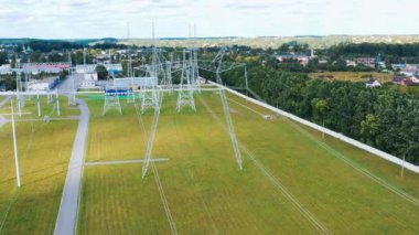 Kırsalda elektrik direkleri var. Sahada beyaz uzun kuleleri olan elektrik santrali. Elektrik dağıtımı. Hareket kamerası geri.