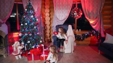 Çocuklar Noel ağacıyla oturma odasında. Noel Baba 'yı görmek için pencereye koşan küçük kızlar. Evde yeni yıl kutlaması.