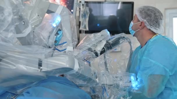 クリニックの医療ロボット近くの専門外科医 医用制服の医師が支援するロボット機器による最小侵襲手術 — ストック動画