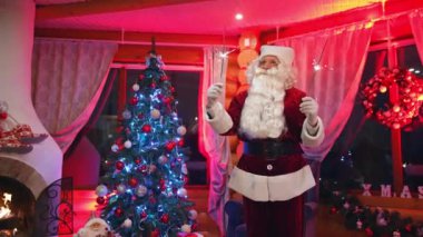 Mutlu Noel Baba 'lar Noel süslemeli odada. Noel Baba, kırmızı kostümlü sakallı, Noel ağacının yanında duruyor. Elinde Noel ışıkları olan otantik Noel Baba.