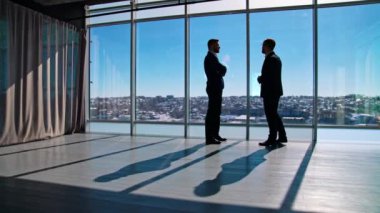 İki adamın iş görüşmesi. Takım elbiseli girişimciler pencere kenarındaki geniş ofis odasında iş konuşuyorlar..