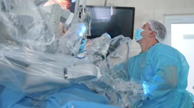 Geleceğin robotu ameliyathanede. Modern tıbbi cihazın yanındaki doktor. Tıbbi monitörün arka planında mikro cerrahi işlemi gösteren robotik cerrahi.