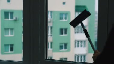Şehrin evindeki pencereleri yıkama işlemi. Yüksek bina arka planında fırça ve özel sıvıyla cam pencereyi temizleyen bir adamın silüeti..
