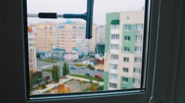 Şehrin camını temizliyorum. Ev fırçası tutan ve pencereyi dışarıdan temizleyen bir adam. İçeriden bak. Kentsel binalar.