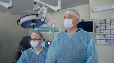 Ameliyathanede profesyonel cerrahlar var. Tıbbi üniformalı ve maskeli erkek doktorların portresi klinikte ameliyat yapıyor..