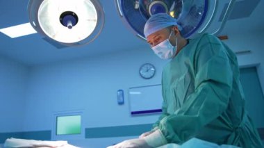 Plastik doktor arka planda tıbbi lambalar üzerinde çalışıyor. Tıp uzmanı modern klinikte liposuction prosedürü uyguluyor. Mavi ışık.