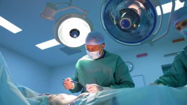 Klinikte estetik ameliyat. Tıbbi üniformalı profesyonel bir doktor ameliyat sırasında hastanın karnında çizgiler çizer. Anestezi altında ameliyat masasında yatan hasta..