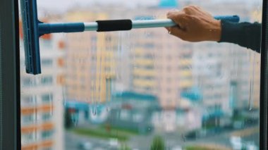 Elinde temizlik fırçası olan el, pencereyi yıkıyor. Şehirdeki yüksek katlı bir binanın dışından plastik pencere temizliği. Düz görünüm.