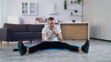 Genç adam evde antrenman yapıyor. Adam bir paspasın üzerinde oturuyor ve karantina döneminde egzersiz yapmaya çalışıyor. Evde antreman yapmanın zorlukları.