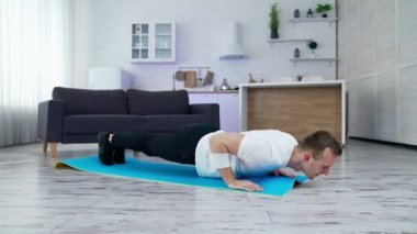 Evde sporcu eğitimi. Beyaz tişörtlü ve siyah pantolonlu bir genç odada paspasın üzerinde egzersiz yapıyor. Yan görüş. Kilitleme sırasında spor.