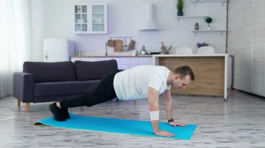 Sporcu, mutfakta egzersiz yapıyor. Kilitleme sırasında evdeki paspasın üzerinde spor yapan genç bir adam. Sağlık ve sağlıklı yaşam tarzı.