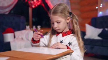 Noel ağacı arka planında resim yapan küçük bir kız. Noel 'den önce şirin bir çocuk Noel Baba' ya resim çiziyor. Odada parlak ışıklar olan yeni yıl ağacı..