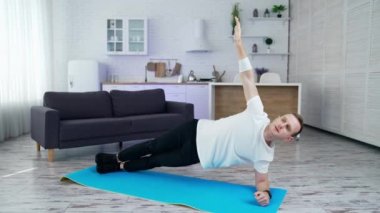 Genç adam evde antrenman yapıyor. Mutfak arka planında hasırla egzersiz yapan bir adam. İzolasyon sırasında vücut şeklini korumak için çok çalışan bir adam..