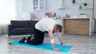 Adam antrenmanını evde yapıyor. Paspaslı genç bir adam mutfak arka planında esneme egzersizi yapıyor ve sırtını uzatıyor. Kilitleme sırasında eğitim.