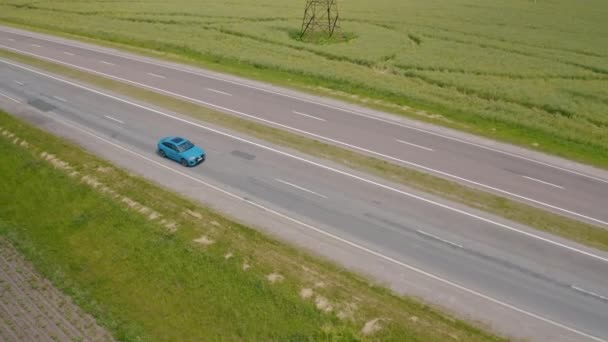 高速道路で運転する美しい青い車 グリーンフィールドの背景にある道路を移動する高級電気自動車 スローモーション エアリアルビュー — ストック動画