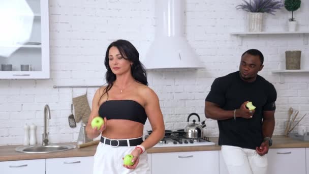 家にいる白人女性と黒人男性 アフリカ人の男が後ろに立って彼女を見ている間 リンゴと美しいスポーティな女性のジャグラー — ストック動画