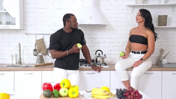 スポーツカップルが自宅で会話をする キッチンテーブルに座って 男性と話している白人女性 新鮮なリンゴを食べる複数の民族カップル 健康的な食事 — ストック動画