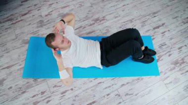 Evde erkek eğitimi. Formda kalıyorum. Beyaz tişörtlü ve siyah pantolonlu genç adam paspasın üzerinde egzersiz yapıyor. Spor ve sağlık. Üst görünüm.