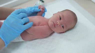 Yeni doğmuş bebek doktorda. Doktor, klinikte doğumdan sonra bebeğin sağlığını kontrol ediyor. Sağlık çalışanı genel kontrol yaparken hastane masasında yatan tatlı bebek..