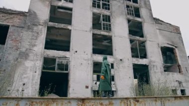 Maskeli ve kimyasal koruyucu giysili bir laboratuvar teknisyeni kuru zeminde yürüyor ve çevreye bakıp kirliliği düşünüyor. Ekolojik felaket kavramı