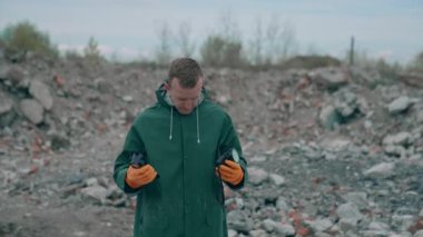 Virolog adam koruyucu kostümünü ve gaz maskesini çıkarırken atık alanı kirliliğinin yanında duruyor ve felaketin boyutuna bakıyor.