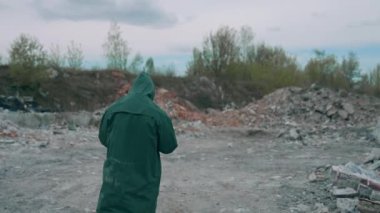Koruyucu kostümlü ve gaz maskeli bir virolog atık alanı kirliliğinin yakınında yürüyor ve felaketin boyutuna bakıyor. Ekolojik afet kavramı