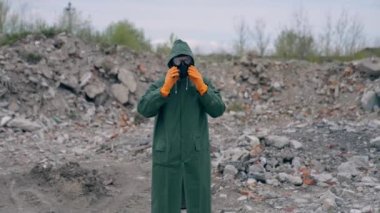 Mahvolmuş bina geçmişiyle ilgili güvenlik kıyafetli bir ekolojist. Gaz maskeli ve koruyucu elbiseli kişi, kimyasal saldırıdan sonra tehlikeli bir yerde duruyor.