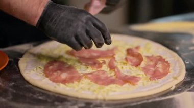 Restoranda pizza yapma süreci. Geleneksel İtalyan pizzası yapma süreci. Şef üstüne hamon ve peynir koyuyor.