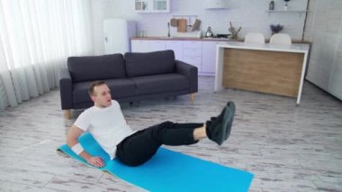 Sağlıklı yaşam tarzı adamı vücudunu evde eğitirken bacak kaldırıyor. Güçlü erkek karantinada çalışıyor. Tam uzunluk