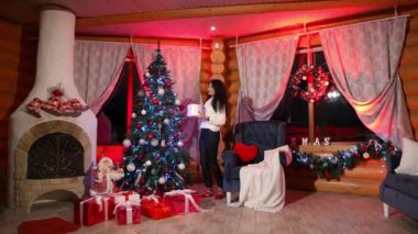 Aile Noel için rahat dairelerde hazırlanıyor. Güzel esmer kadın çocuklarıyla Noel ağacı süslüyor. Yeni yıl kutlaması konsepti