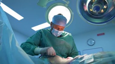 Yağ aldırma. Abdominoplasti yapan üniformalı bir cerrah. Ameliyathanede bir hastanın karnından cerrahi müdahaleyle yağ alınması.