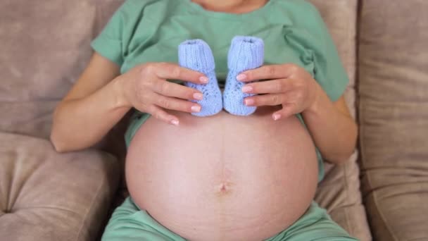 漂亮的孕妇 家里穿着婴儿鞋 怀孕妇女准备生儿育女 抱着小宝宝鞋靠近腹部 — 图库视频影像