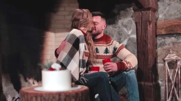 爱喝茶的夫妻 穿着针织圣诞毛衣的年轻人和美女坐在壁炉边 男人亲吻他的女朋友 浪漫的夜晚 — 图库视频影像