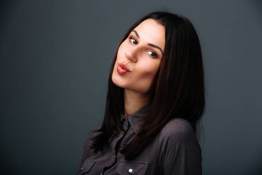 Uzun siyah saçlı ve siyah gömlekli kadın. Siyah tişörtlü, uzun siyah saçlı bir kadın sade bir arka plana karşı güvenle duruyor..