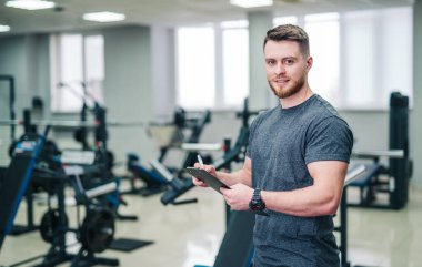 Spor Salonu Bekleme Tableti, Spor İzleme Teknolojisi. Bu fotoğrafta bir adam, spor salonunda elinde bir tabletle fitness izleme teknolojisini kullanırken yakalanıyor..