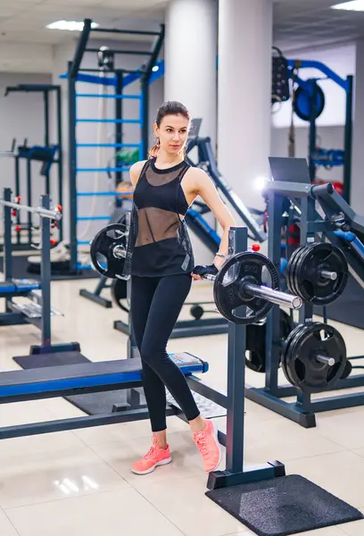 Woman Standing by Gym Machine. An active woman stands confidently next to a gym machine, ready for an intense workout.