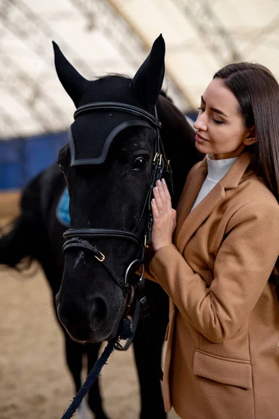 Woman Standing Next to Black Horse. A woman stands calmly next to a majestic black horse, forming a bond between human and animal.