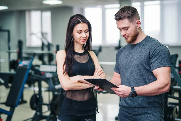 Man and Woman Check Gym Clipboard for Fitness Goals and Progress