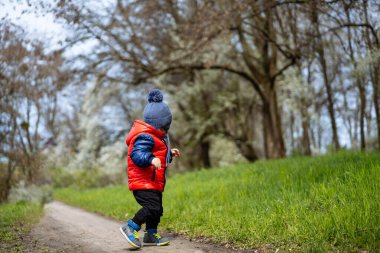 Küçük çocuk bahar günü annesiyle birlikte parkta yürüyüşe çıkıyor..