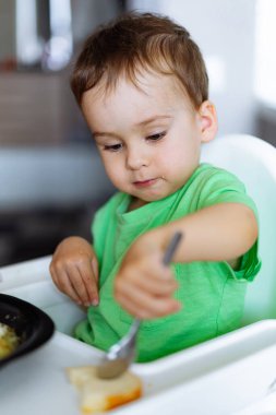 Şirin küçük çocuk kahvaltısını yapıyor ve mutfakta eğleniyor.