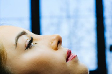 Genç kadın güzellik salonunda uzanıyor ve güzellik uzmanının makyajını yapmasını bekliyor..