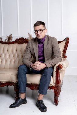 Ceketli ve gözlüklü adam kanepede oturuyor..