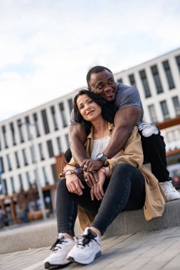 Mutlu genç çift merdivenlerde oturup birbirlerine sarılıyorlar.