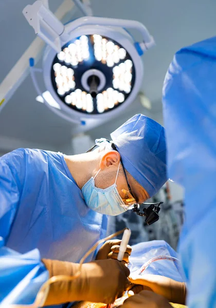 Surgeon and assistant in blue surgical gowns perform complex operation on patient in the operating room