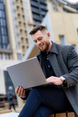 Adam bankta oturur ve dizüstü bilgisayarıyla çalışır..