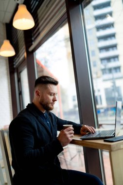 Genç adam kafede dizüstü bilgisayarda çalışıyor..