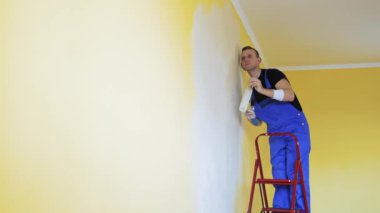Yeni apartman yenileme odasında genç bir adam. Fırça silindiri ile çalışan yakışıklı ressam evini yeniliyor.