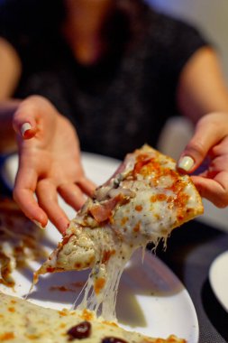 Kadın tabaktan bir dilim peynirli pizza alıyor.